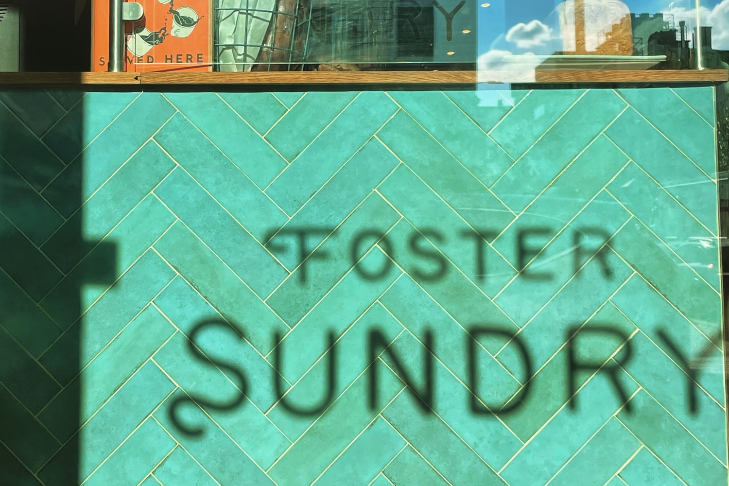 Foster Sundry lettering cast across the green tiled counter, seen through the shop window.
